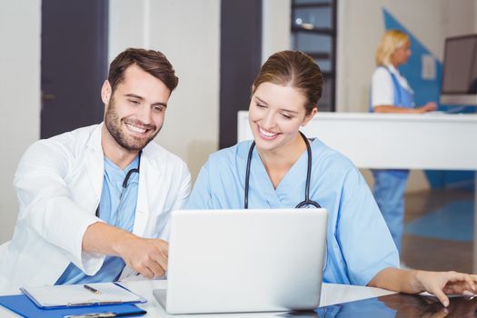 Happy doctors using laptop while discussing at desk in hospotal