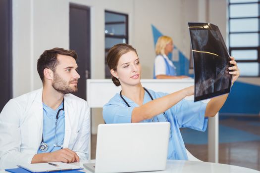 Female doctor examining X-ray with colleague sitting at desk in hospital