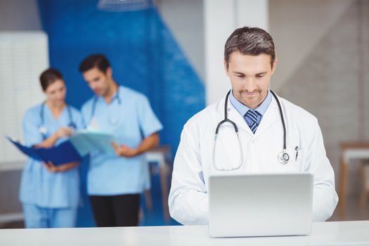 Doctor working on laptop with colleagues discussing on background