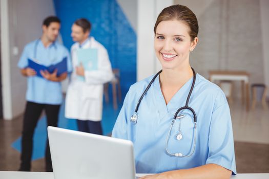 Portrait of happy female doctor with laptop and colleagues discussing on background