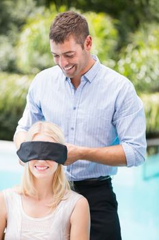 Smiling man blindfolding woman at poolside