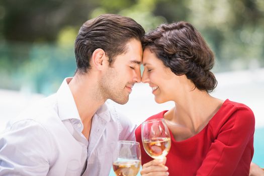 Romantic couple with eyes closed while holding white wine at poolside