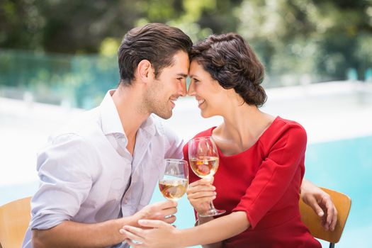 Romantic couple holding white wine while sitting at poolside