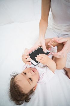 Midsection of mother holding mobile phone while playing with baby on bed at home
