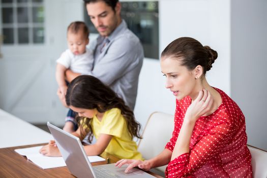 Mother working on laptop with daughter studying at home