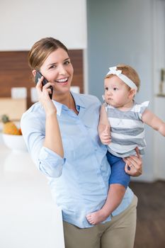 Happy woman using mobile phone while carrying daughter by table at home