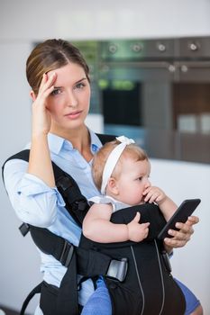 Tensed woman with mobile phone carrying baby girl at home