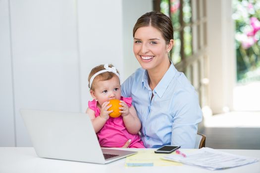 Happy woman sitting with baby by table at home