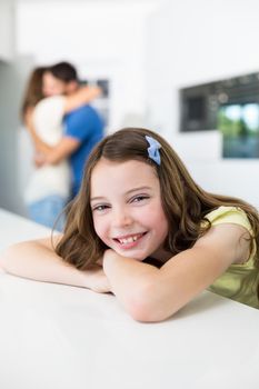 Portrait of smiling girl leaning on table against embracing parents at home 