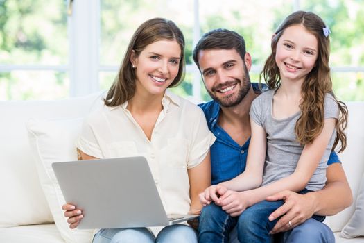 Portrait of family with laptop sitting on sofa at home 