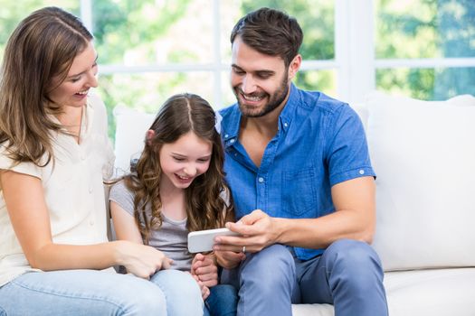 Family looking at smart phone while sitting on sofa at home 