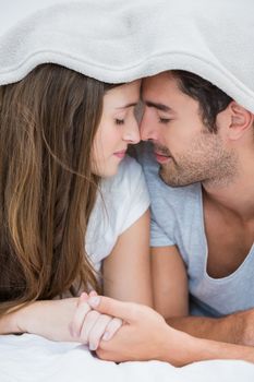 Close-up of couple romancing under blanket on bed at home 