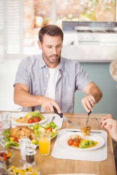 Man serving meat in plate while having lunch with family at home