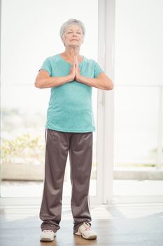 Senior woman with hands clasped performing yoga at home