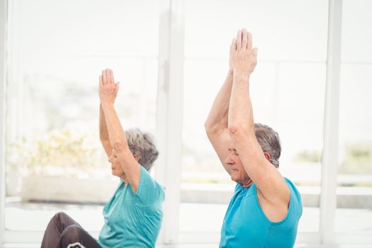 Senior couple performing yoga with arms raised at home