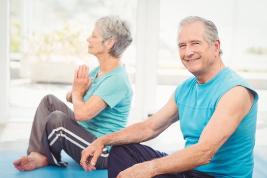 Portrait of smiling senior man sitting beside wife performing yoga at home