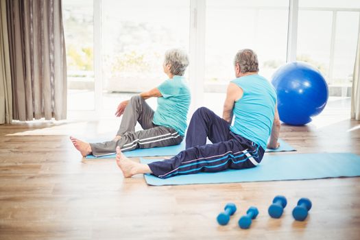 Rear view of couple doing yoga on exercise mat at home