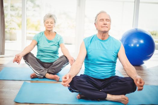 Senior couple meditating with eyes closed on exercise mat at home