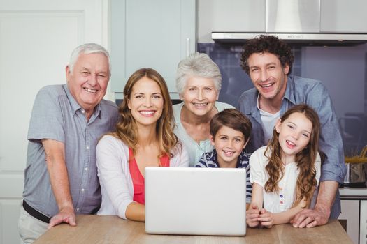 Portrait of smiling happy family with laptop in kitchen at home