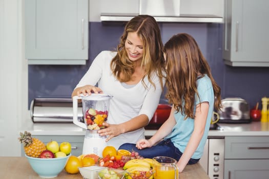 Happy mother and daughter preparing fruit juice at table in kitchen