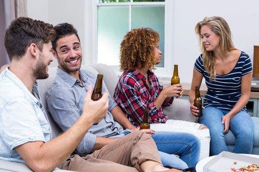 Multi-ethnic friends smiling while enjoying beer at home