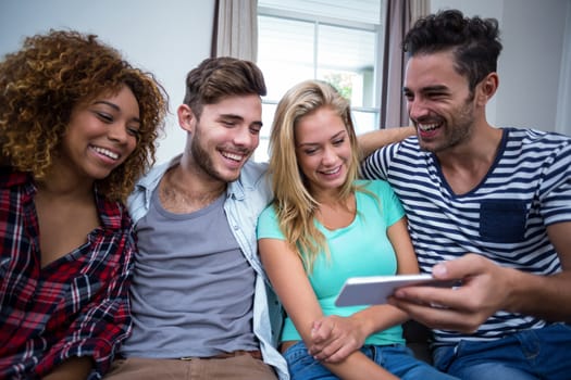 Happy young friends looking in mobile phone while sitting on sofa at home