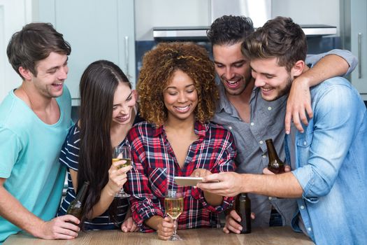 Multi-ethnic friends looking in mobile phone while standing by table in kitchen