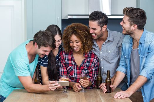Multi-ethnic happy friends looking in mobile phone while standing by table at home