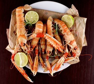 Delicious Grilled Langoustines with Limes and Rosemary Parchment Paper on White Plate and Dark Wooden background. Top View