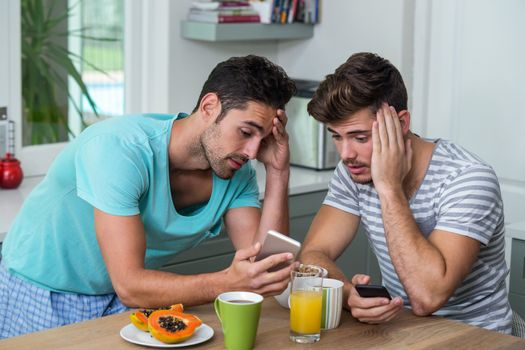 Frustrated male friends using phone while standing at table
