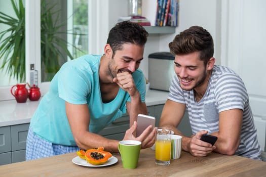 Smiling male friends using phone while standing at table