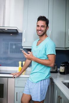 Portrait of smiling young man with phone while standing in kitchen