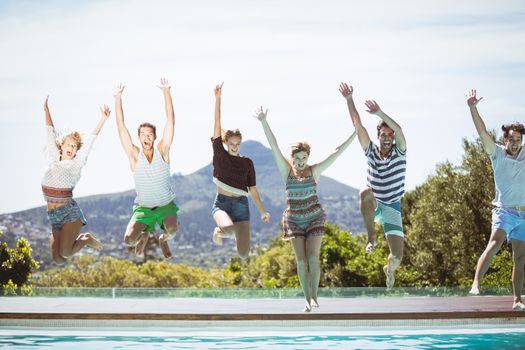 Group of friends jumping in swimming pool with their hands raised