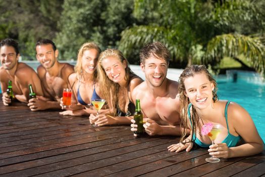 Group of happy friends having drinks at the swimming pool