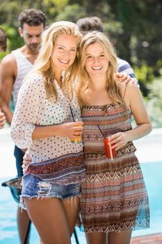 Young women smiling and having juice together while their friends standing behind