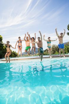 Group of friends jumping in swimming pool with their hands raised