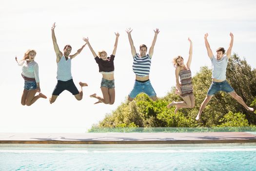 Group of friends jumping at poolside with their hands raised