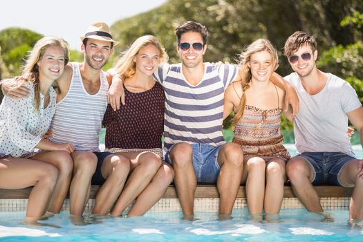 Group of happy friends smiling and sitting side by side at poolside
