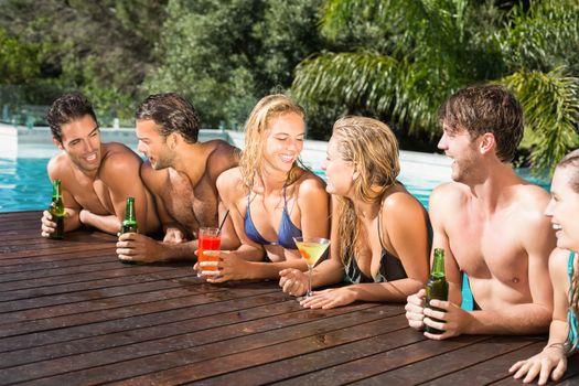 Group of happy friends having drinks at the swimming pool