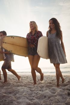 Beautiful friends walking with surfboards on the beach