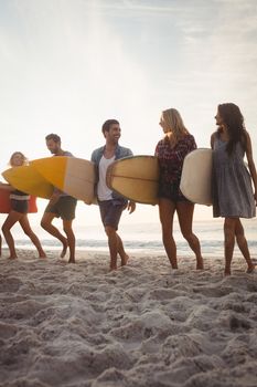 Happy friends walking with surfboards on the beach
