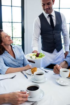 Waiter serving salad to the business people in restaurant