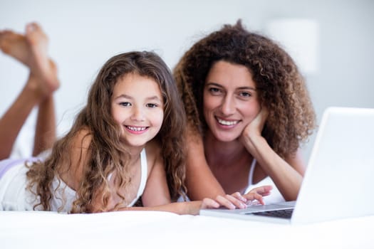 Portrait of mother and daughter using laptop on bed in bedroom
