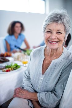 Portrait of senior woman sitting at dinning table and family in background