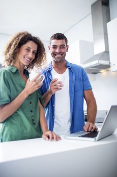 Portrait of couple using laptop while having a cup of coffee in kitchen