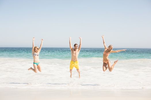 Happy young friends jumping on the beach with arms outstretch