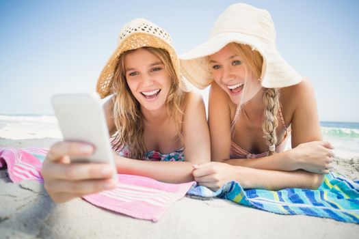 Two happy woman lying on the beach and looking at mobile phone