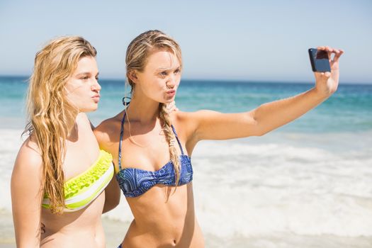 Two friends in bikini taking a selfie at beach