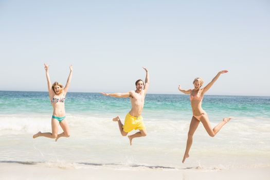 Happy young friends jumping on the beach with arms outstretch