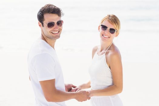 Romantic couple wearing sunglasses holding hands on the beach